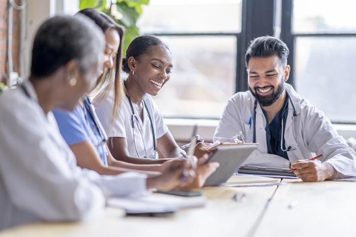 four medical professionals at a table reviewing clipboards and smiling